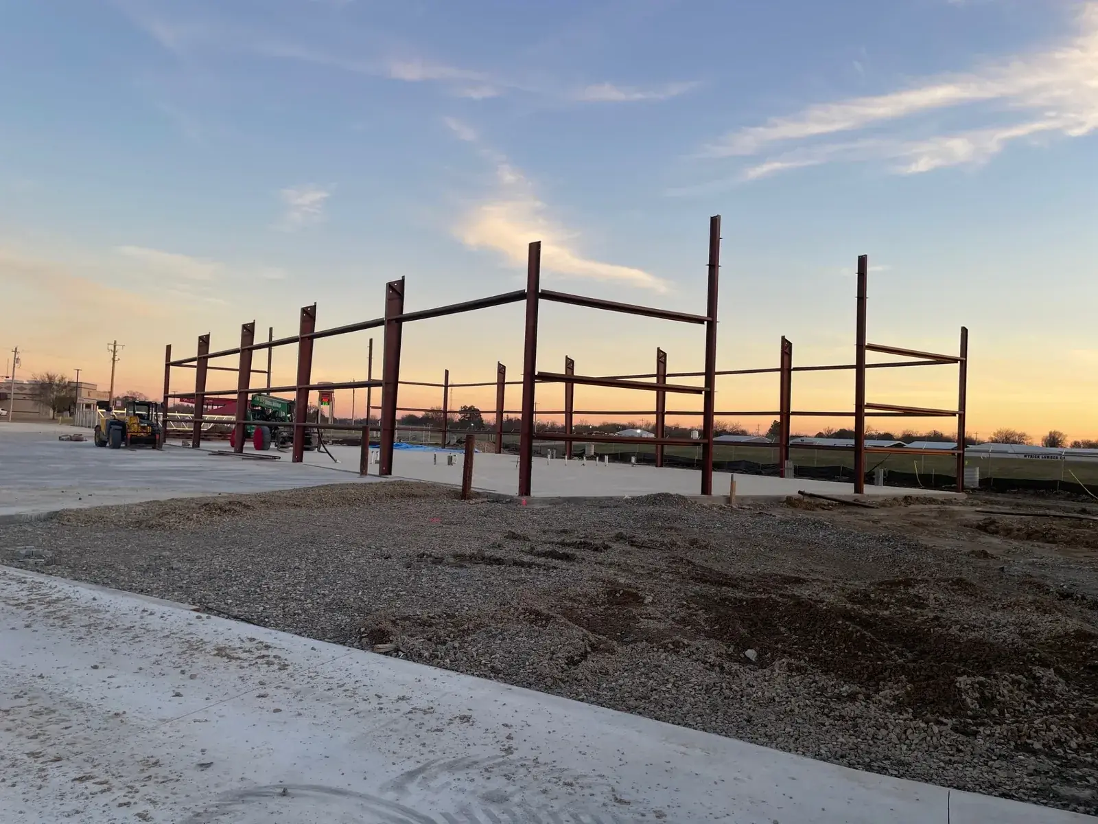 Steel frame erection — UTS BuildPros Primary steel frame erected on a poured concrete slab at dusk, with a telehandler on site — UTS BuildPros metal building contractor, Texas